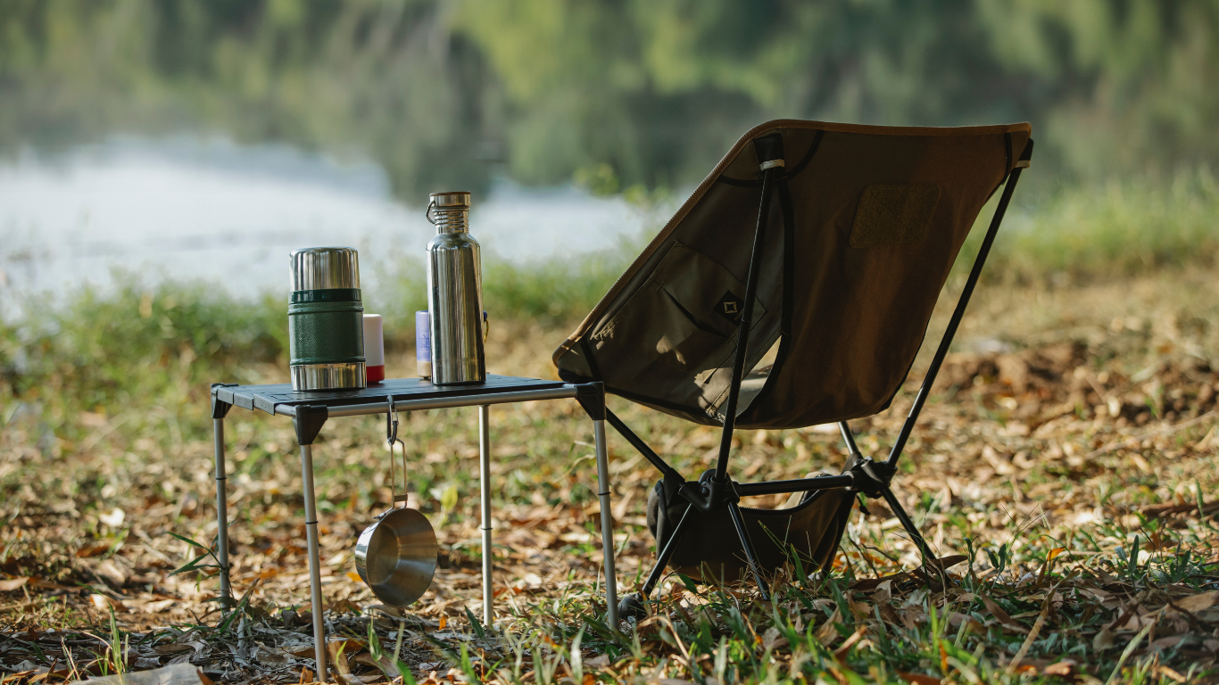 Camping scene: A folding chair sits next to a small table with a thermos and water bottle.