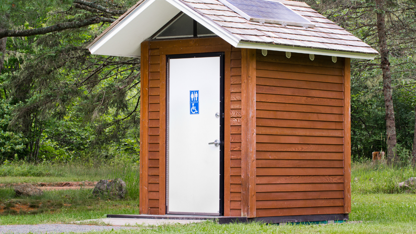 Wooden outhouse with a white door, a sloped roof, and a blue and white restroom sign.