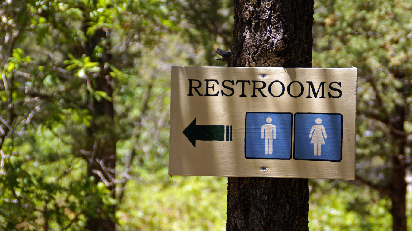 Sign on a tree trunk indicating restrooms with an arrow and gender symbols, set outdoors.