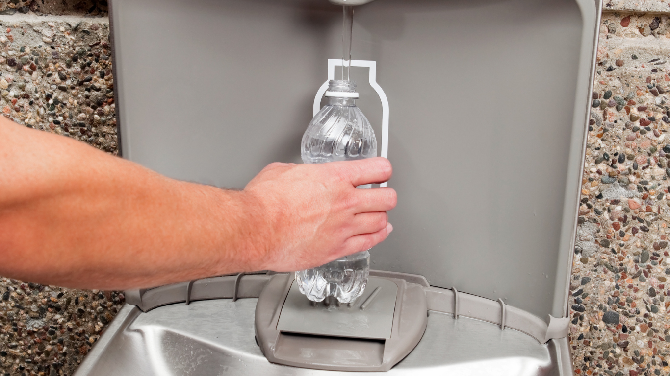 Person filling a clear plastic water bottle from a public water fountain.