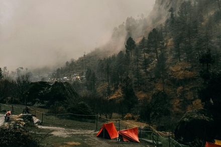 Camping tents in a misty, mountainous landscape with evergreen trees and cloudy skies.