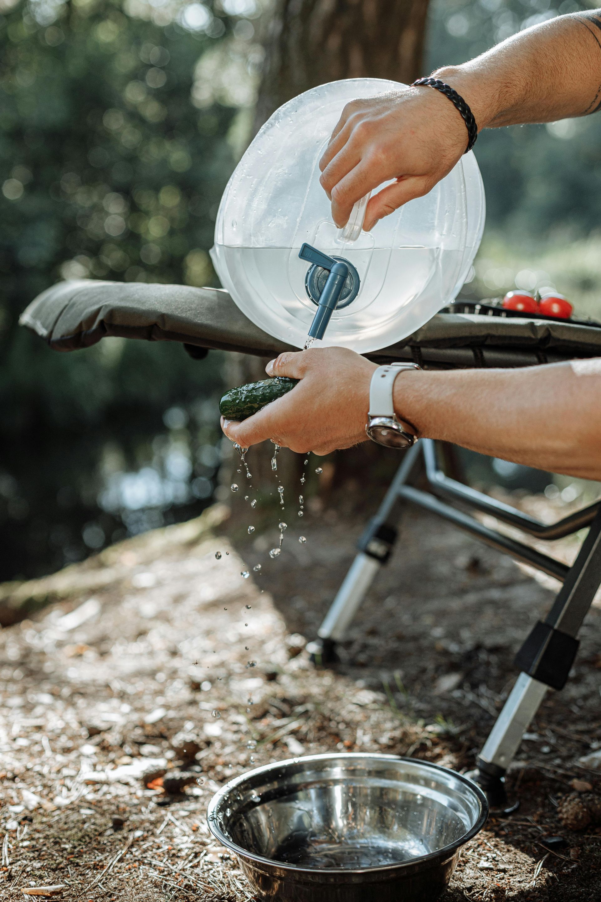 A person is pouring water from a clear collapsible container into a metal bowl, set up outdoors.