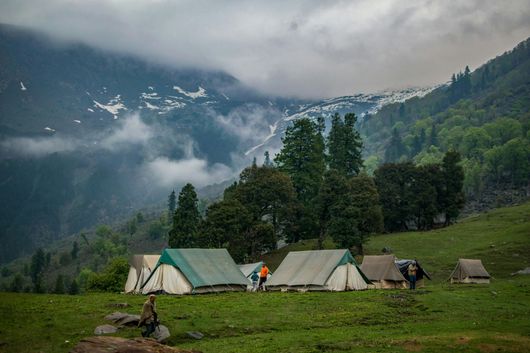 Camping tents in a green meadow with a mountain range in the background.
