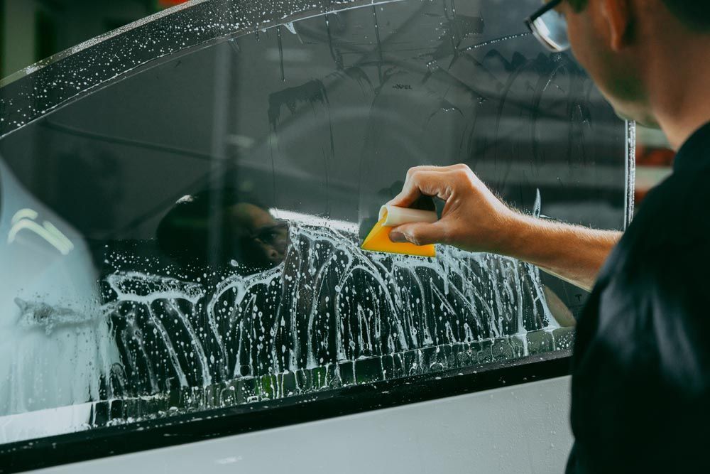 Man applying soapy water to car window with a yellow applicator, preparing for tinting.