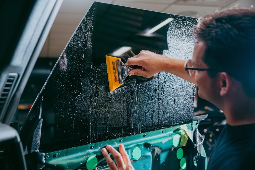Man applying window tint to a car window with a squeegee in a shop.