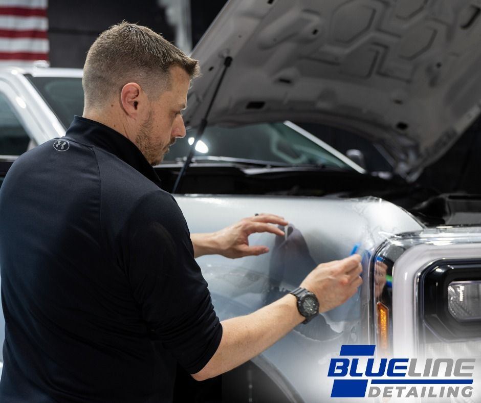 Man applying film to a car's hood in a detailing shop.