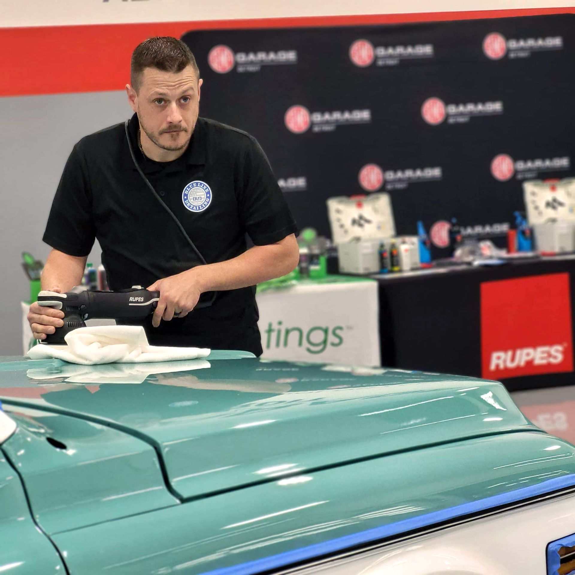 Man polishing a light blue car in a garage.