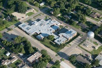 Aerial view of a multi-building structure with a water tower, trees, and residential streets.