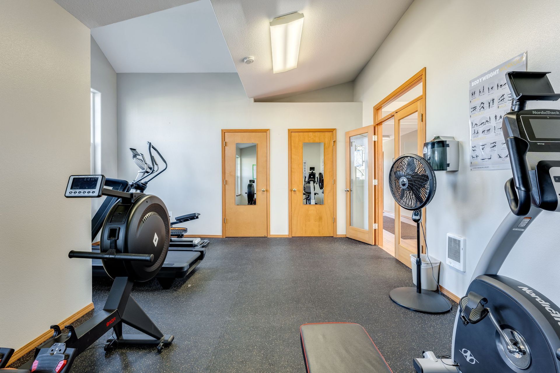 Fitness center with view of doors. Stationary bike to the right, row machine, treadmill and elliptical to the left.