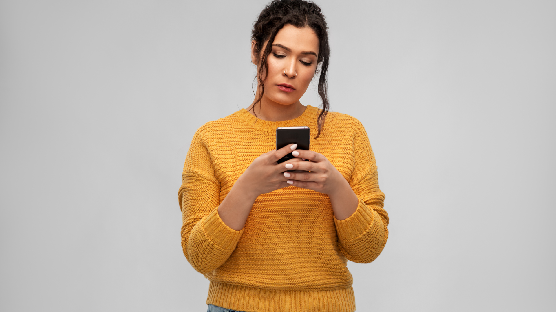 A woman in a yellow sweater is looking at her cell phone.