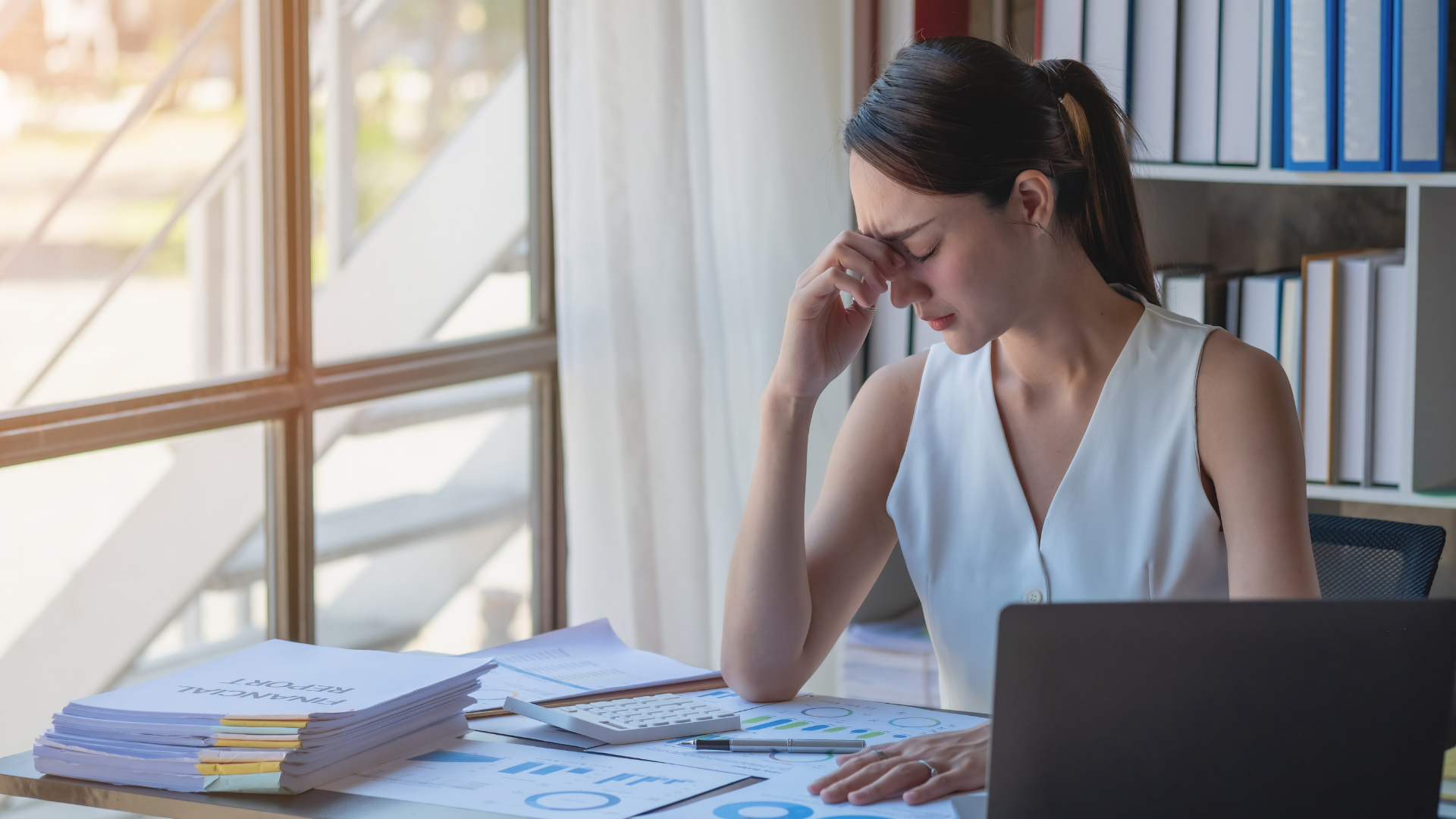 A woman is sitting at a desk with a laptop and a calculator.