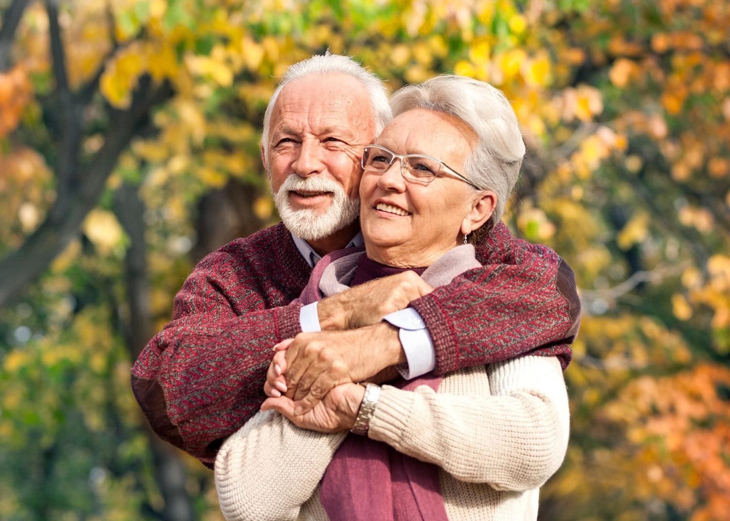 An elderly couple is hugging each other in a park.