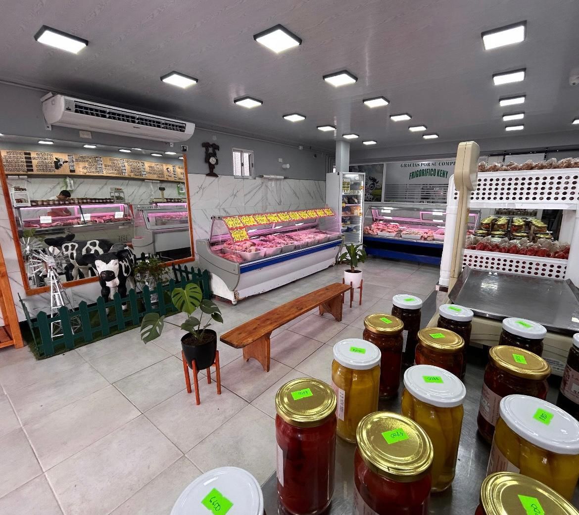 Interior de una carnicería con expositores de carne, estantes con conservas y un banco.