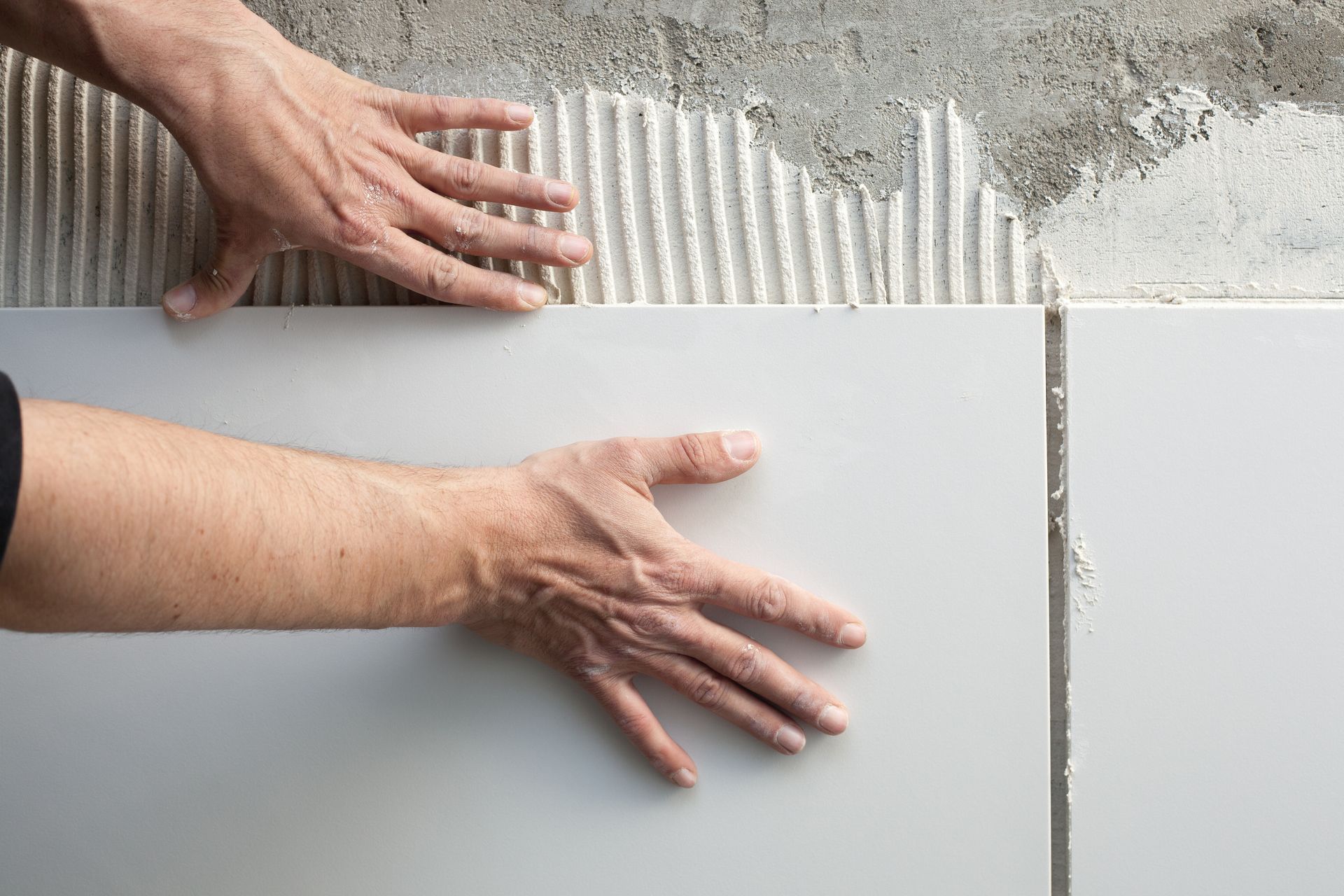 Hands Placing White Tile on a Wall With Mortar — Totally Building and Maintenance in Avoca, NSW