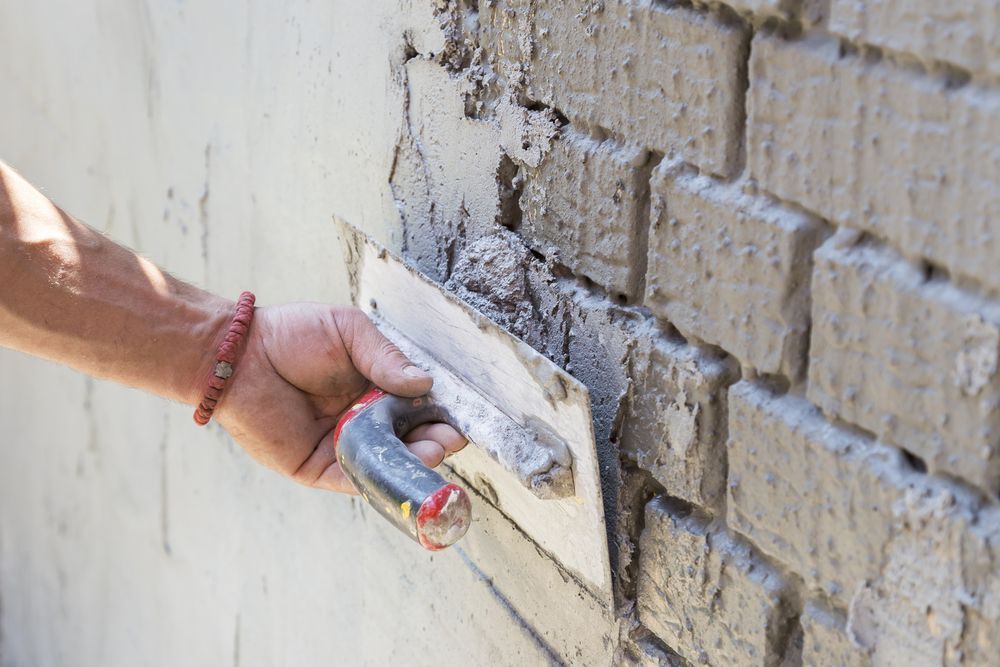 Hand Using a Trowel to Apply Mortar on a Brick Wall — Totally Building and Maintenance in Kincumber, NSW