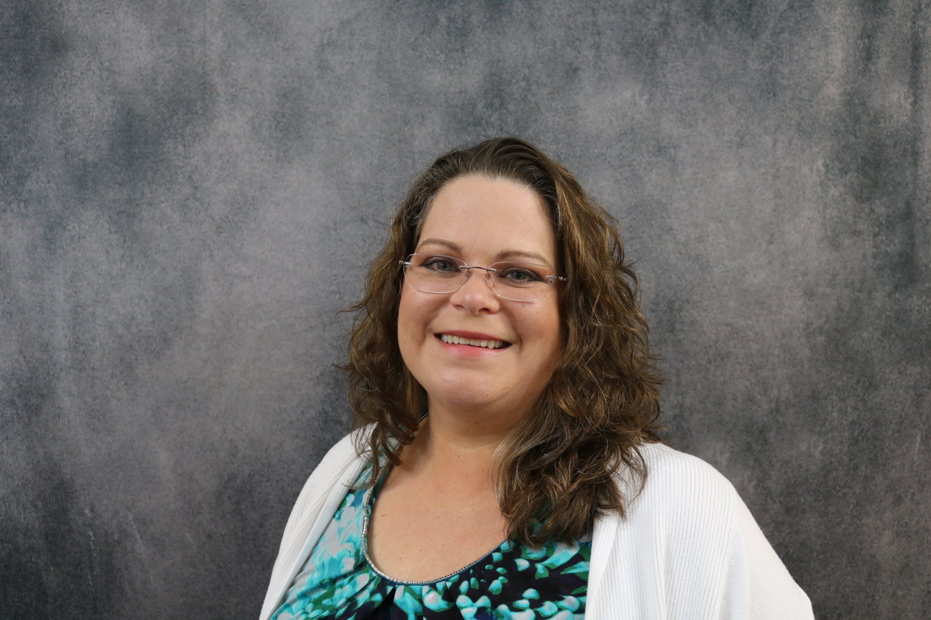 A woman wearing glasses and a blue shirt is smiling for the camera.