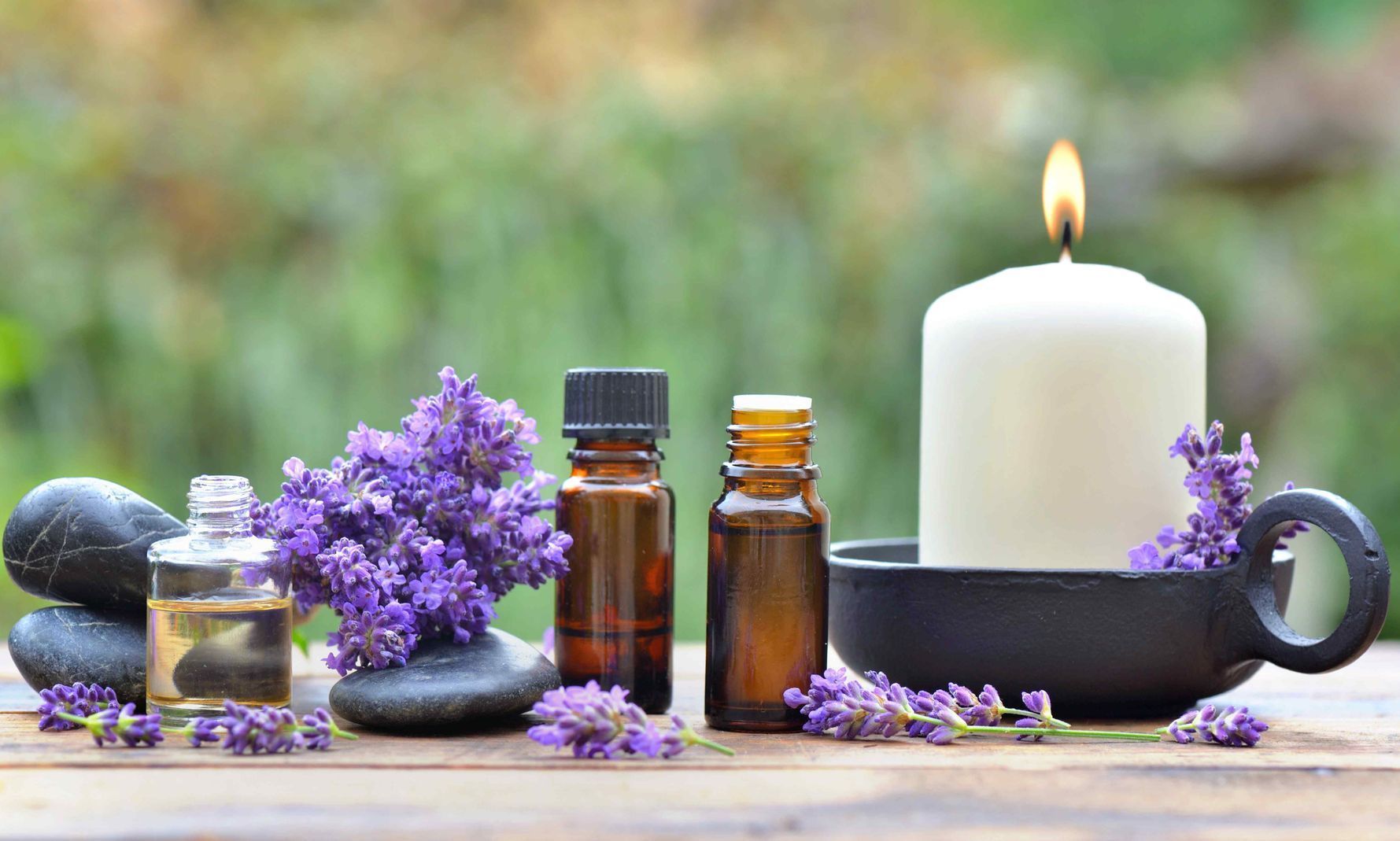 bottles of essential oil among lavender flowers arranged on a wooden table in the garden with candle