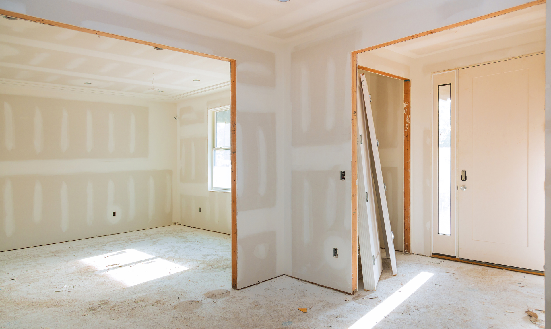 Interior of a room under construction, with drywall walls and wooden door frames.