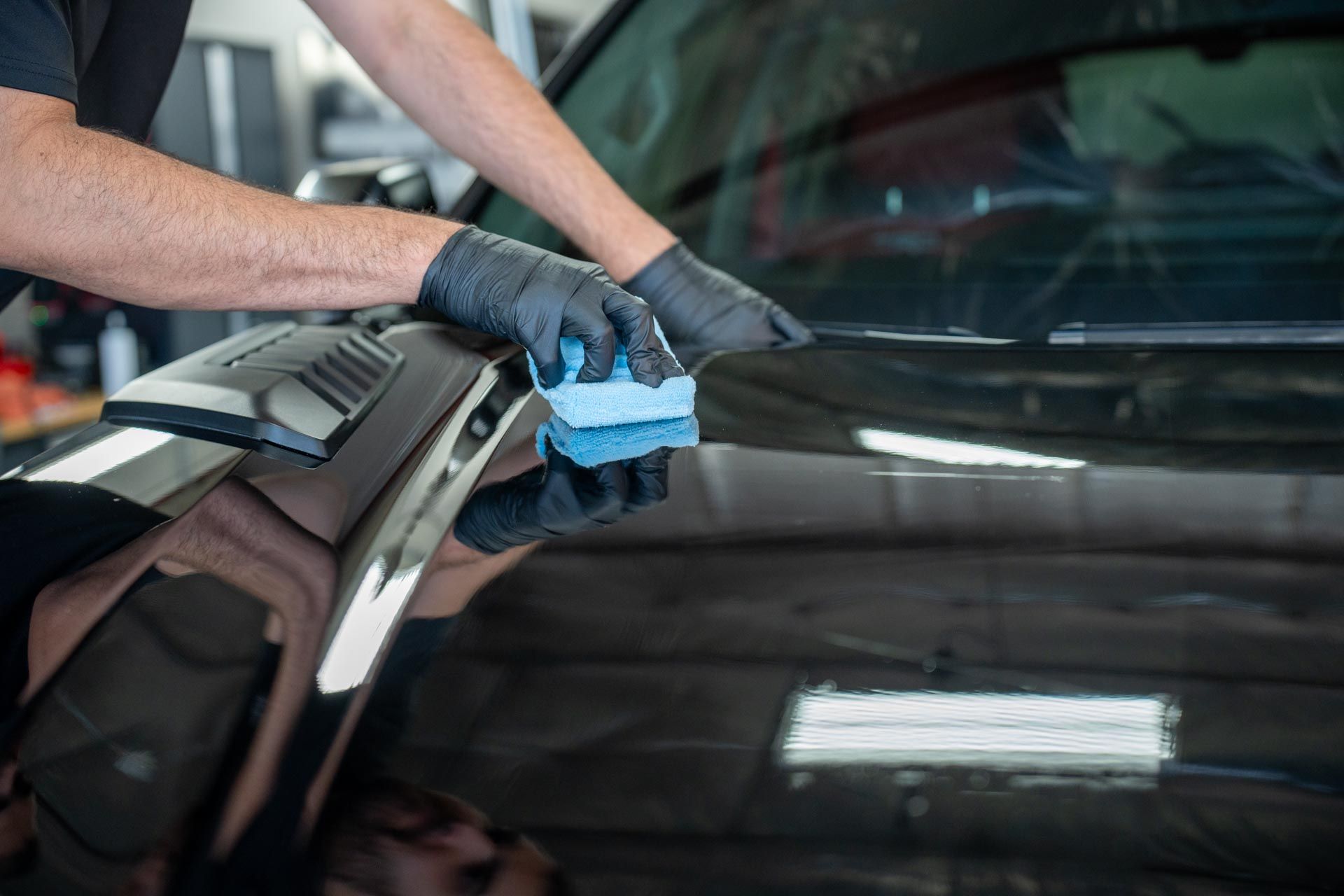 a man wearing black gloves is cleaning a car with a blue sponge