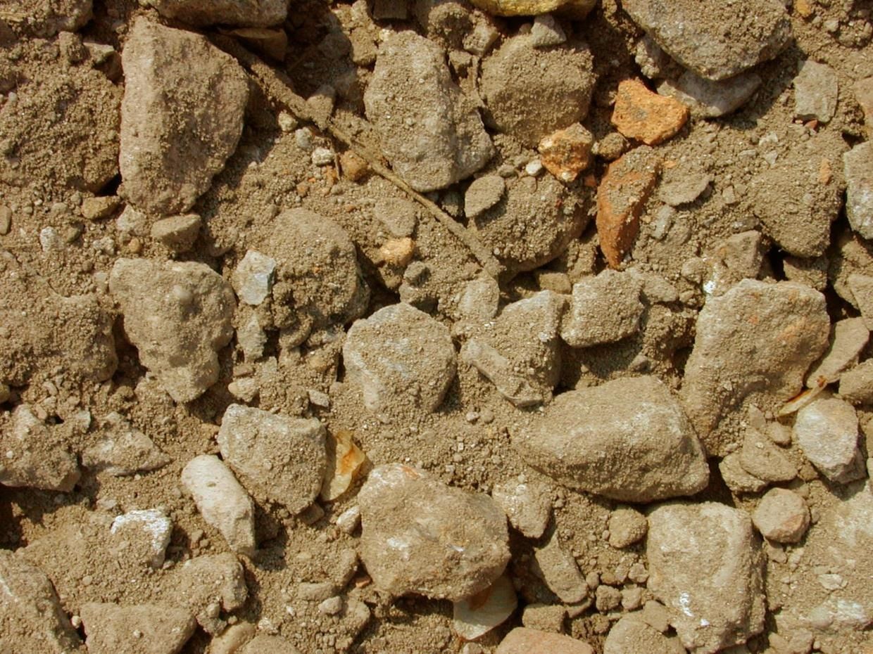 Primo piano di ghiaia e piccole rocce, per lo più beige e marrone chiaro, con alcuni ciottoli più scuri.