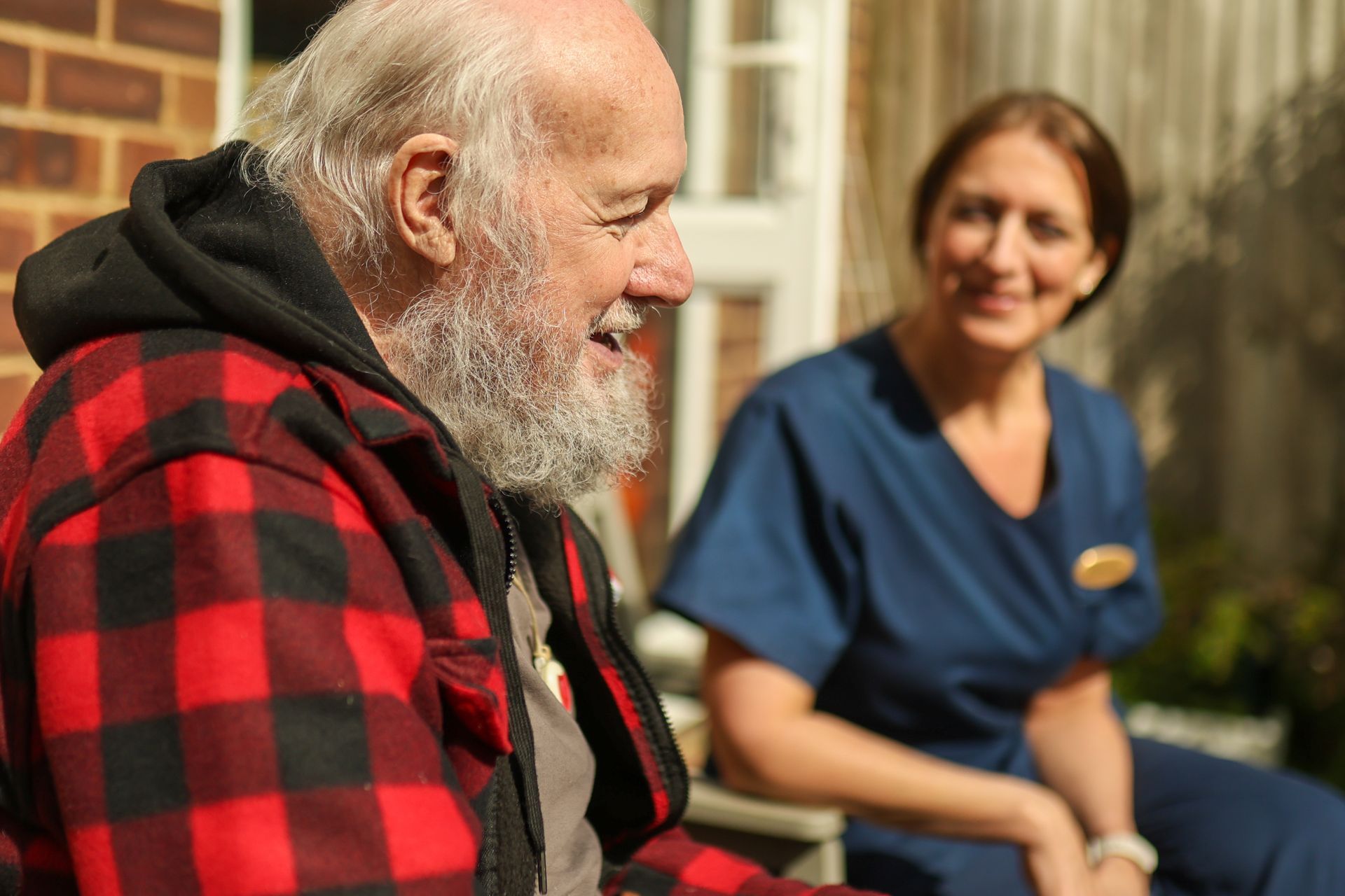 A person wearing a red and black plaid jacket converses with a professional in blue scrubs outdoors.