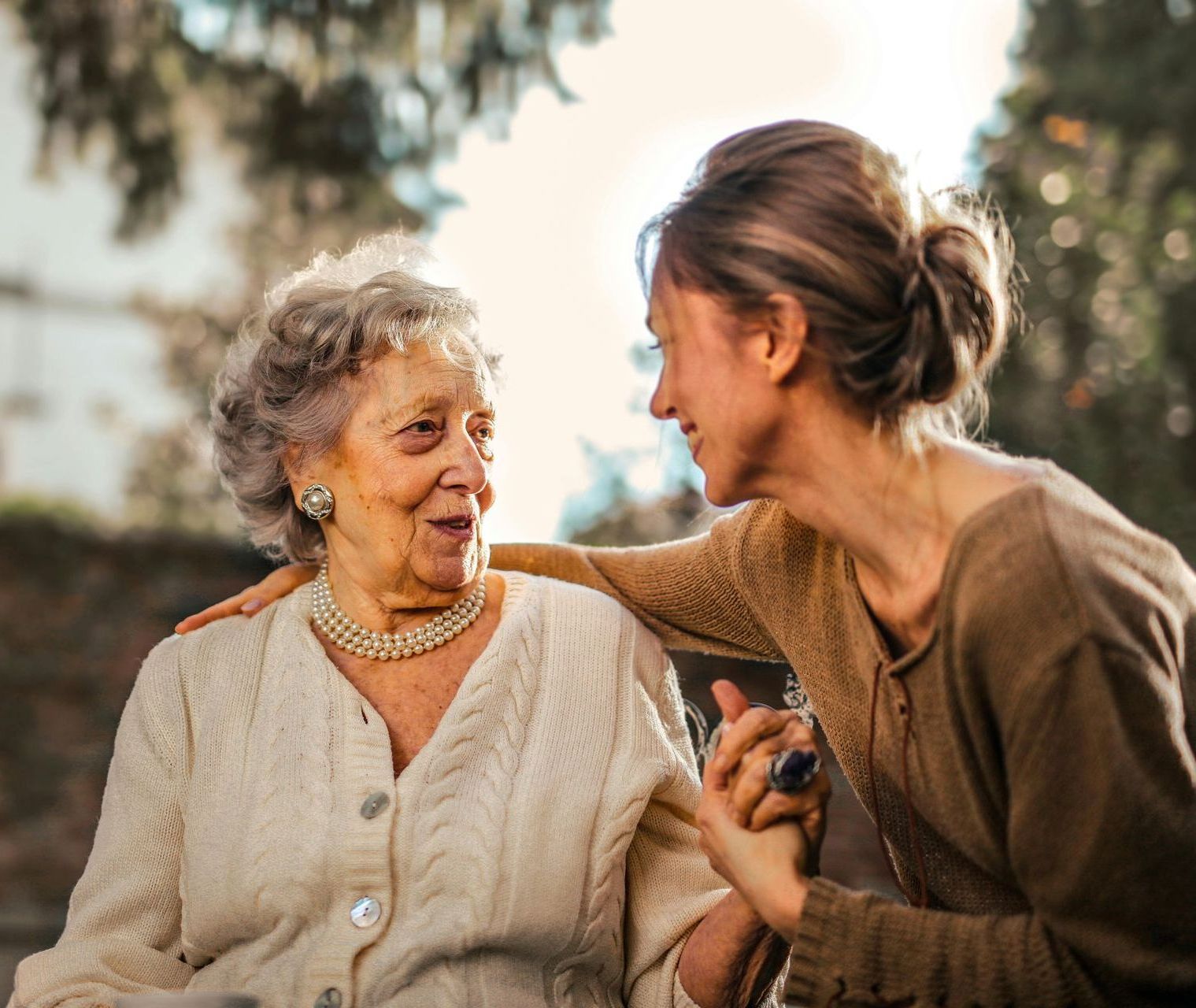 Two people in a sunlit outdoor setting share a gentle, supportive moment while holding hands.