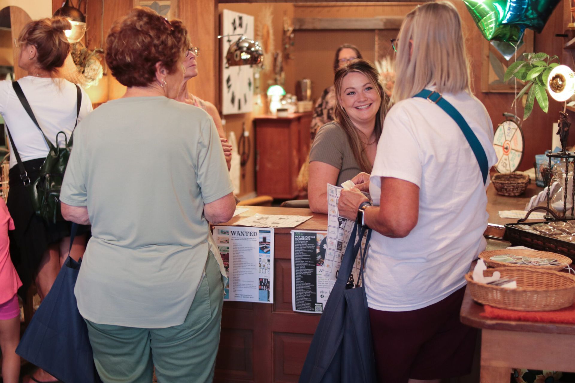 People browsing a store, conversing with a smiling shopkeeper at the counter, various goods on display.