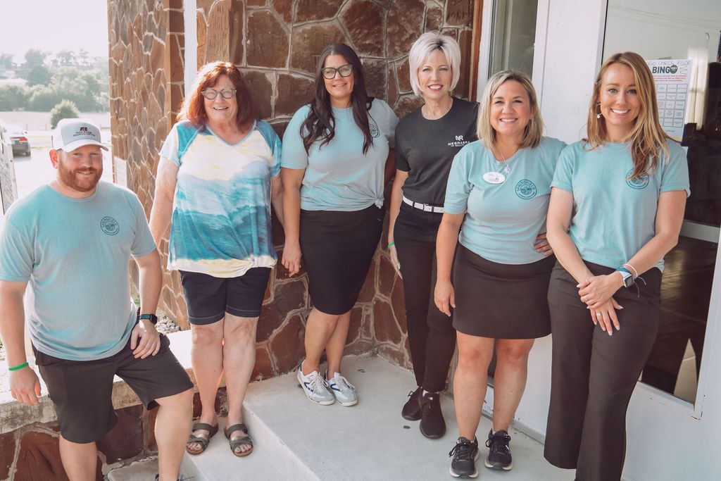 Group of seven people posing outside, wearing matching blue shirts.