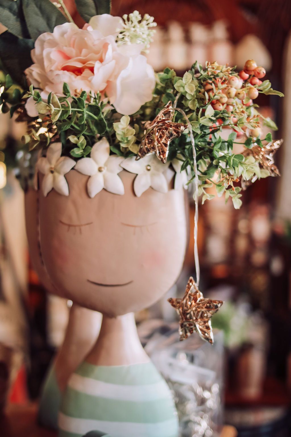 Vase shaped like a child's head, filled with flowers; a gold star dangles from the arrangement.
