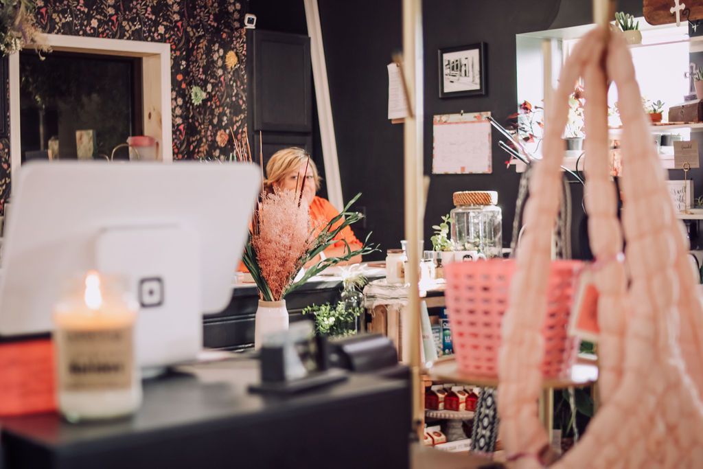 Cash register and customer in a shop, with a pink basket and macrame plant holder in view.