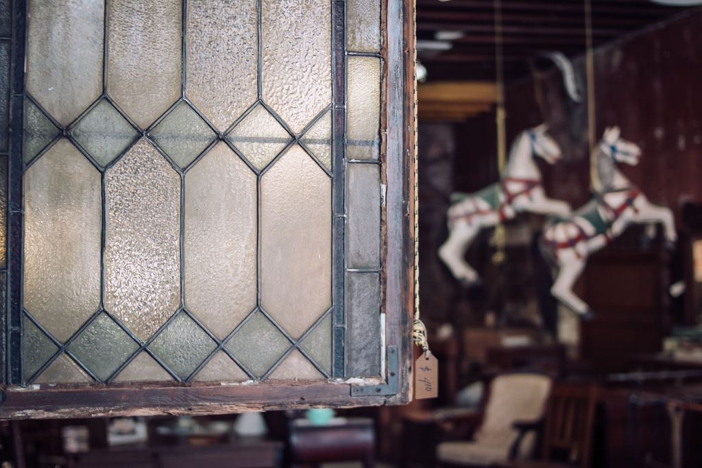 Close-up of a stained-glass window panel; carousel horses and antique furniture blur in the background.
