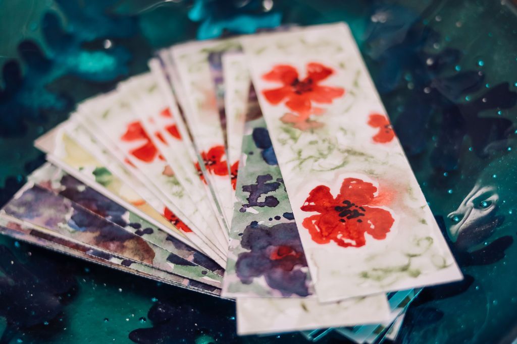 Watercolor poppy bookmarks fanned out on a teal surface.