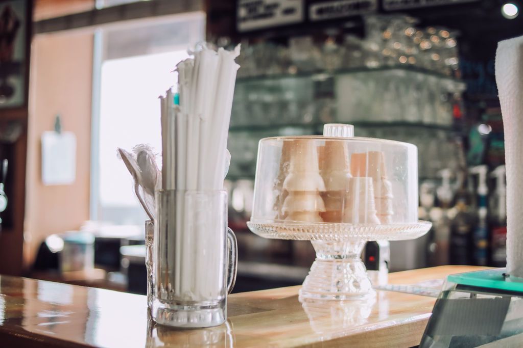 Countertop with straws, cake stand holding cones, and blurred background of a shop.