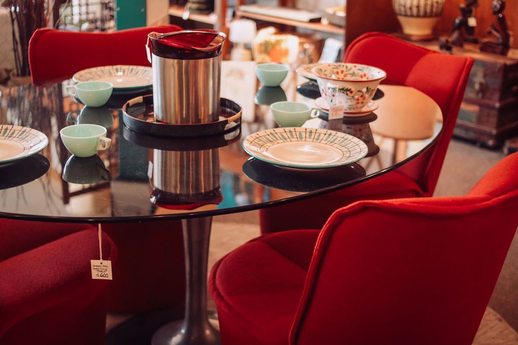Red chairs surround a glass-topped table set with plates and bowls. A metal container sits in the center.