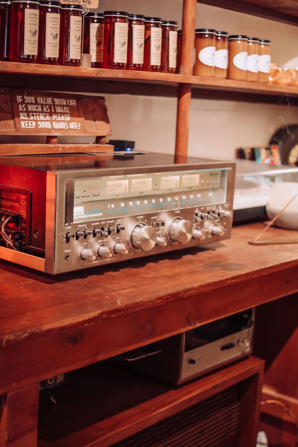 Vintage silver stereo receiver on a wooden shelf, jars of preserves in the background.