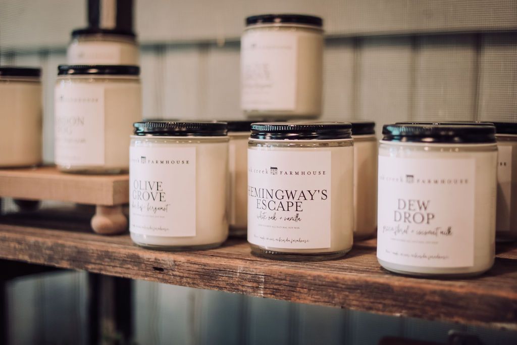 Candles on wooden shelves, labeled with black text on white labels. Jars have black lids.