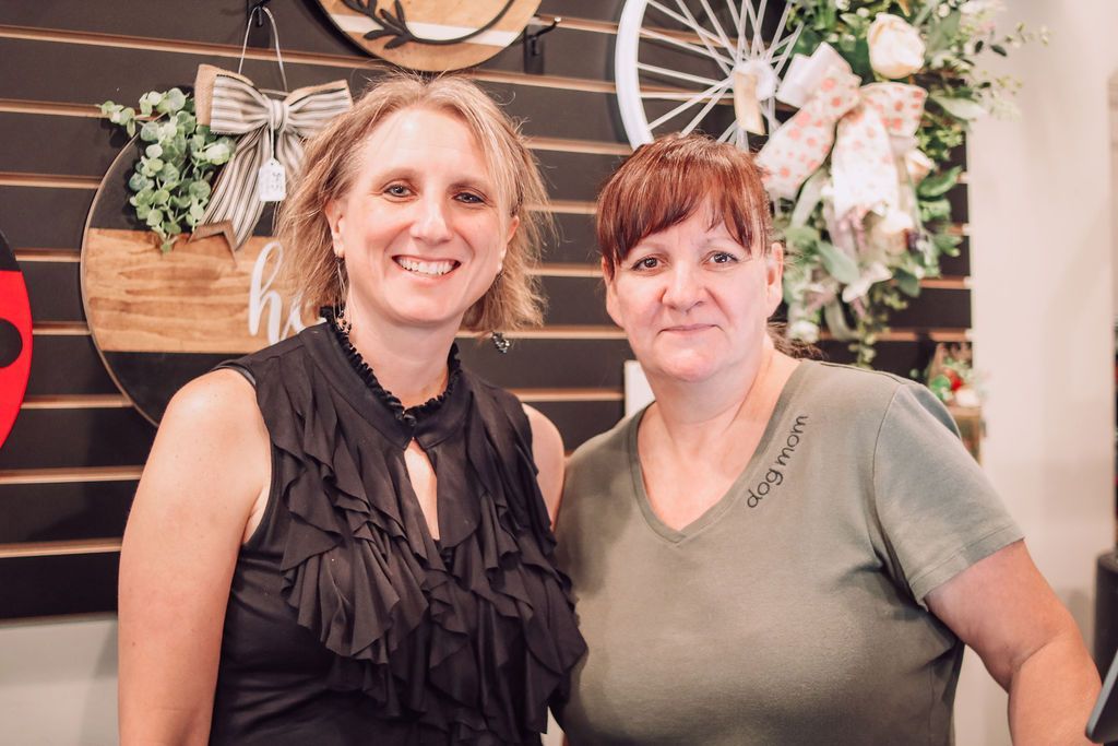 Two women smiling in a shop with decorations. One in black, the other in green.