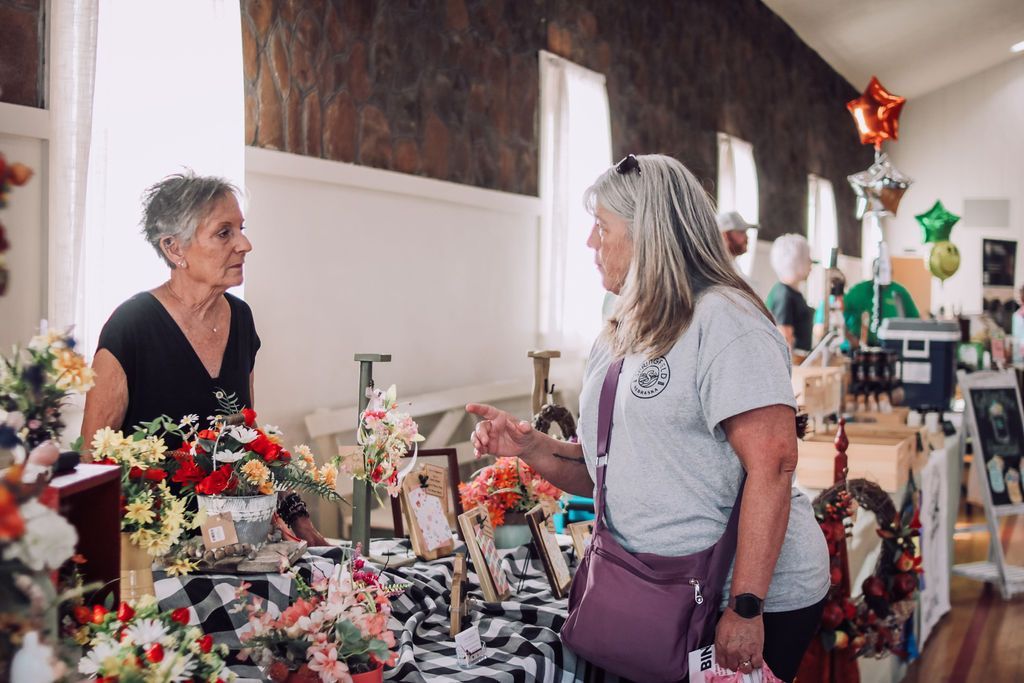 Woman selling flowers at a market, talking to a customer; the setting is indoors with decorative items.