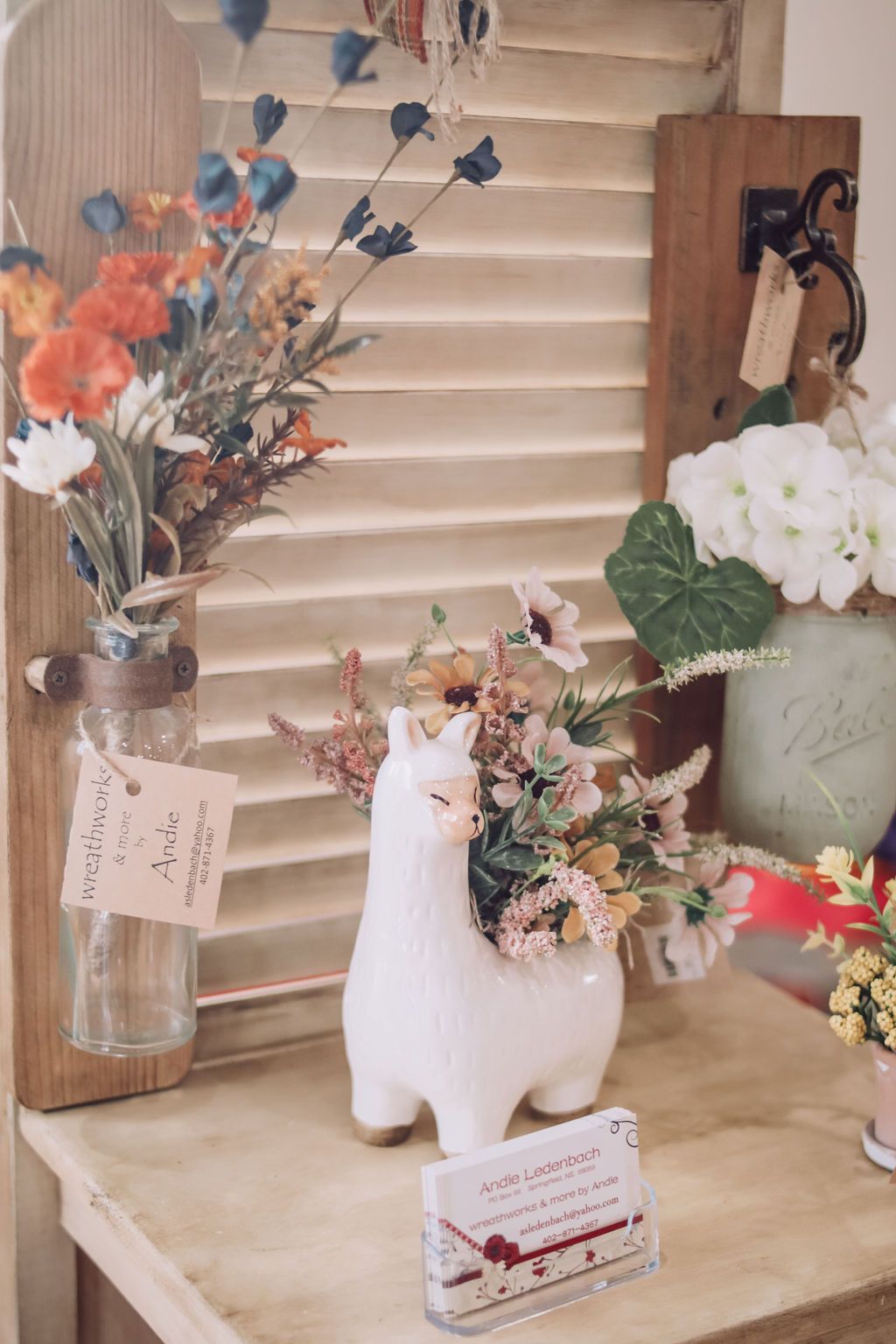 White llama planter with colorful flowers on a wood shelf, next to other floral arrangements.