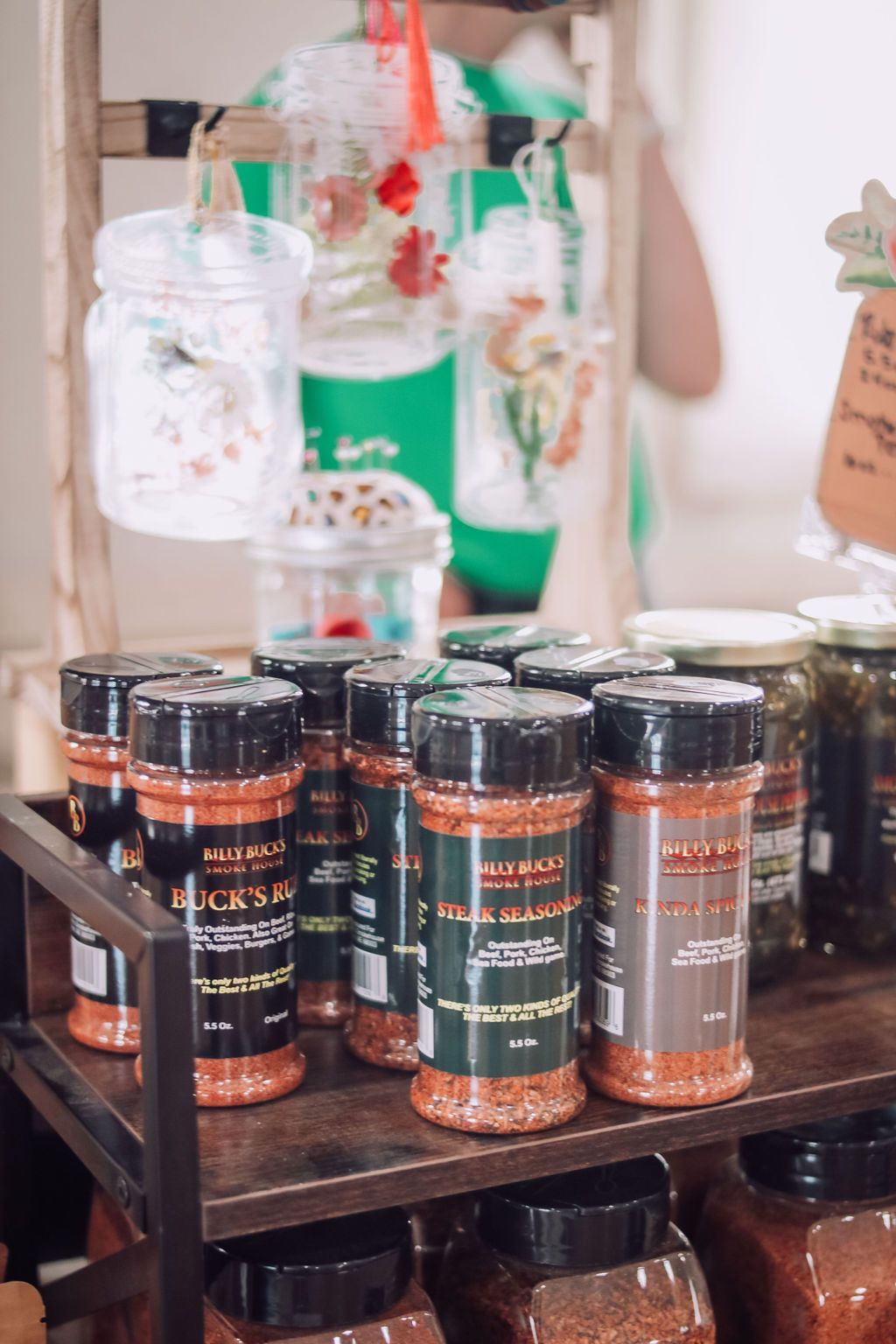 Spice jars on a wooden shelf, with clear containers in the background.