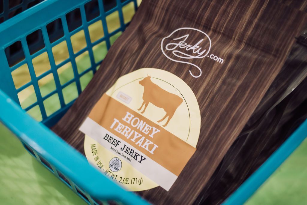 Honey teriyaki beef jerky bag in a blue plastic basket. Brown bag with a cow illustration and 