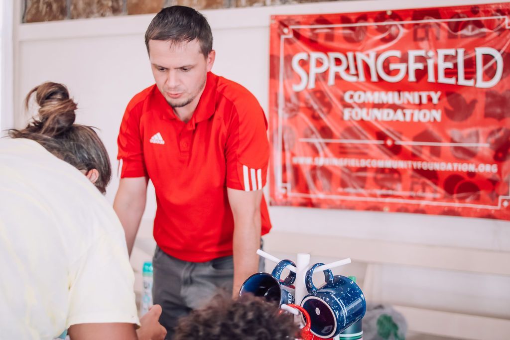 Man in red shirt at Springfield Community Foundation table, looking at objects.