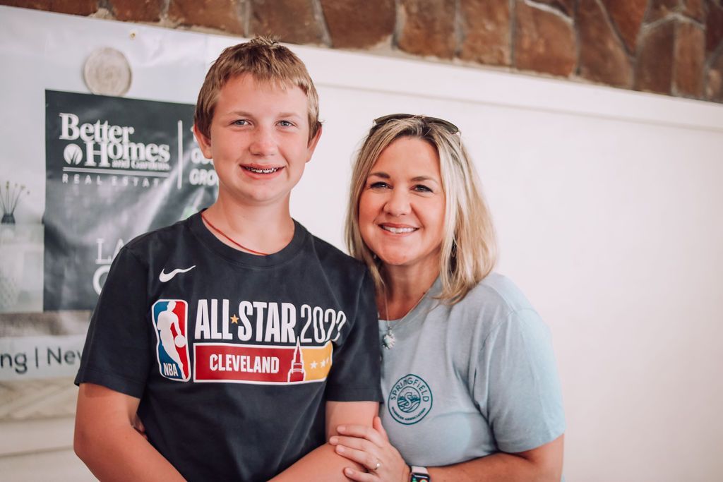 A boy and a woman smile at the camera. They stand in front of a white wall and a Better Homes sign.