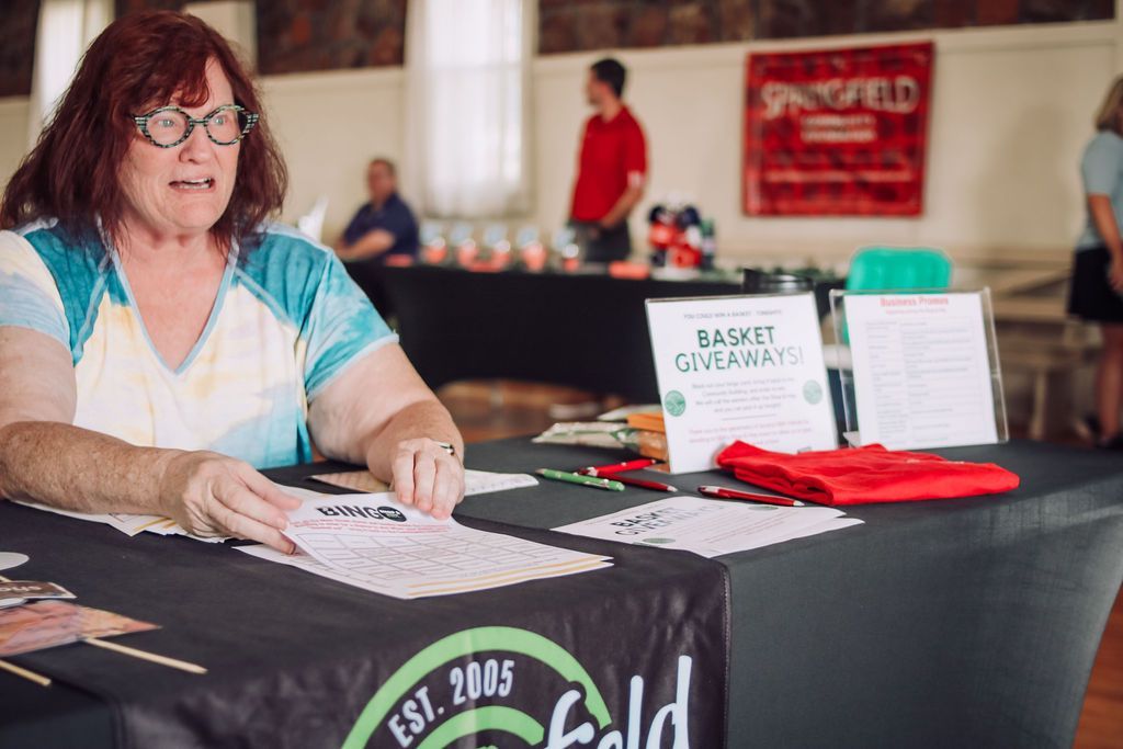Woman at a table with signs; Springfield logo on the table; indoor event.