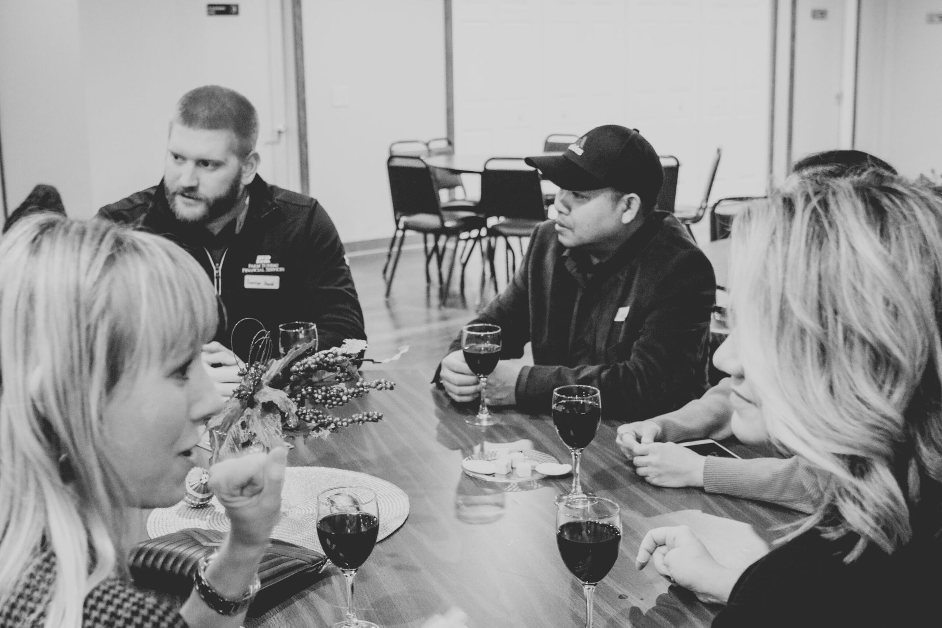 People seated at a table, drinking wine and conversing. Interior setting. Black and white photo.