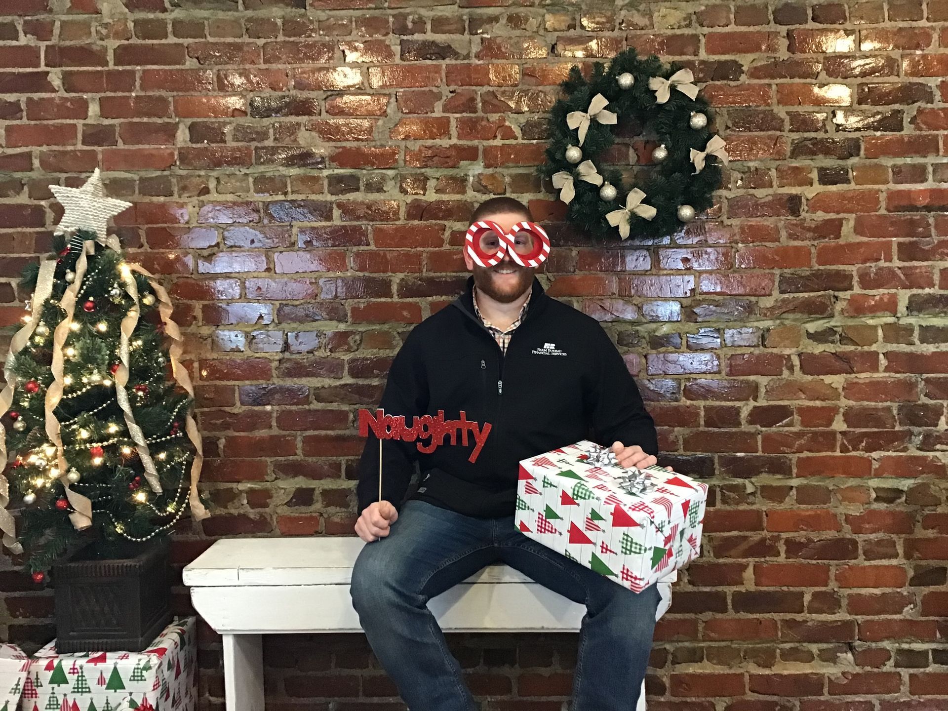 Man in front of brick wall, Christmas tree, and wreath, holding a 