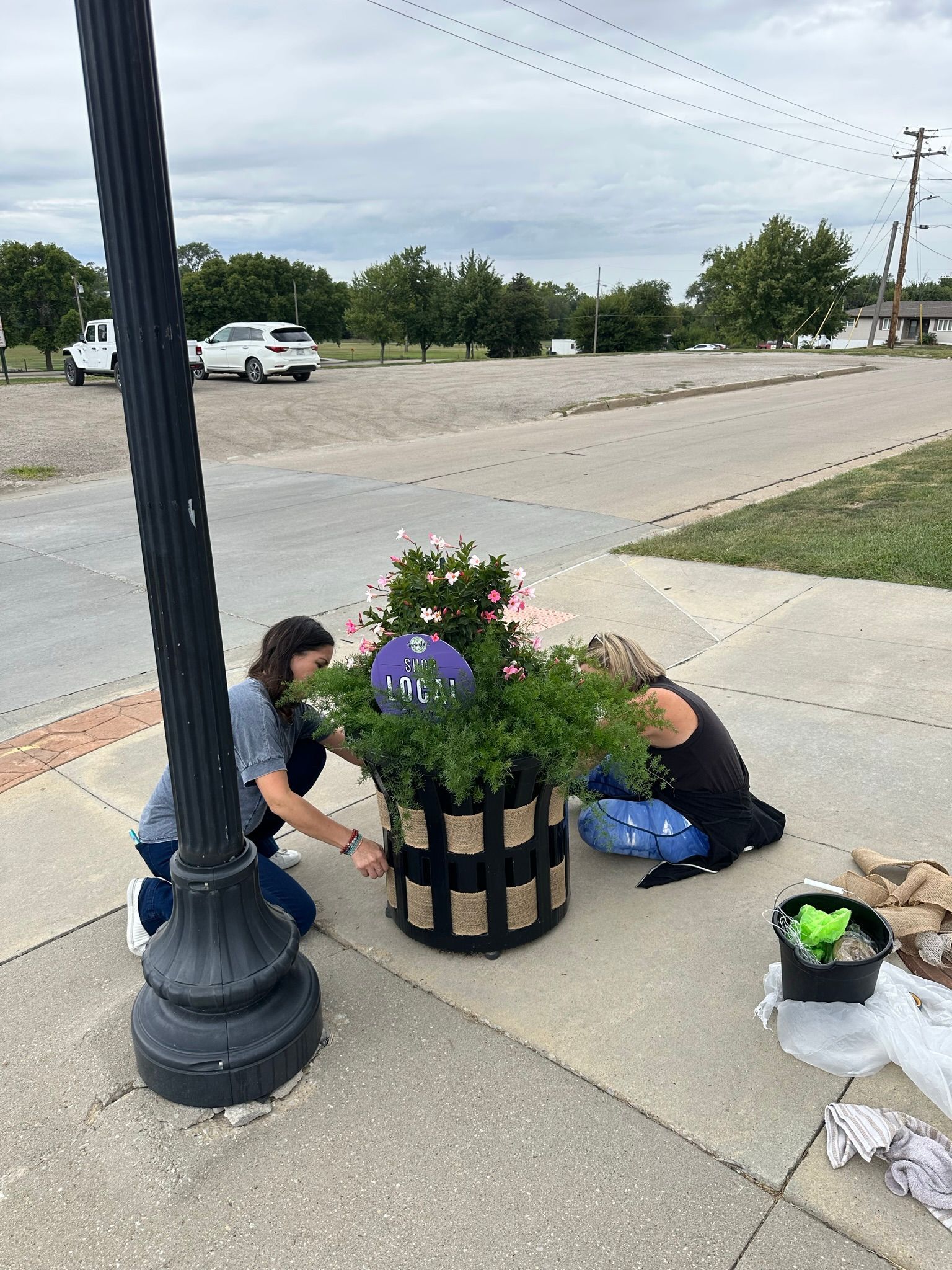 Two people planting flowers in a decorative planter near a street.