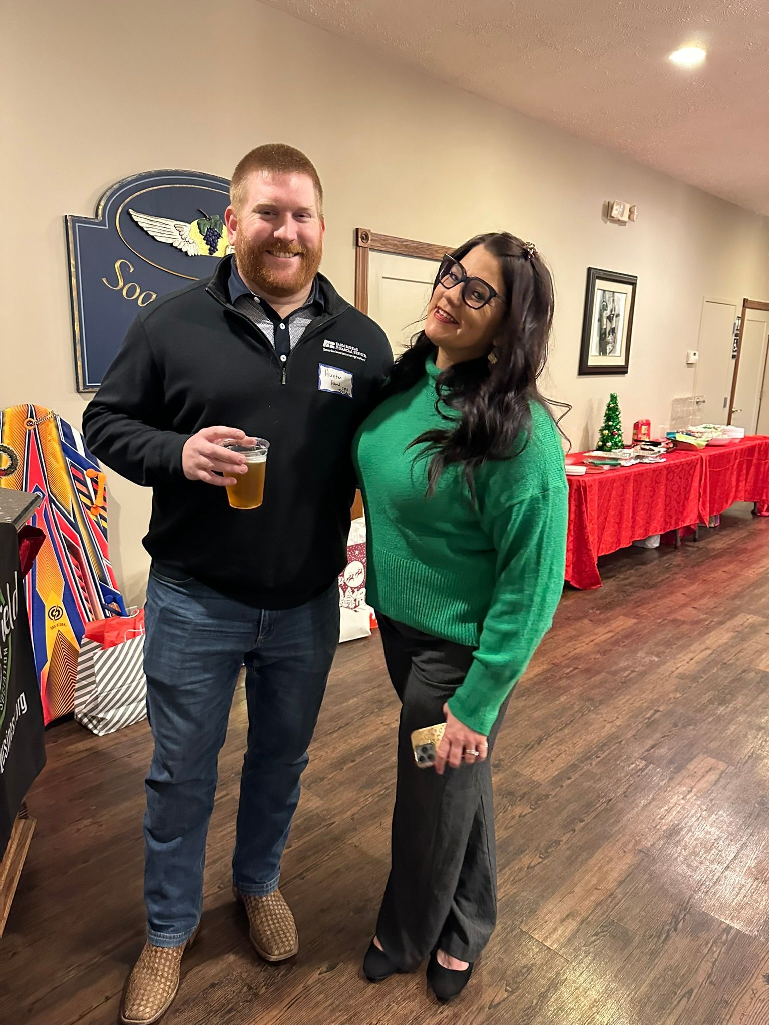 A man and woman smiling at a holiday party. The man holds a beer, and the woman leans in.