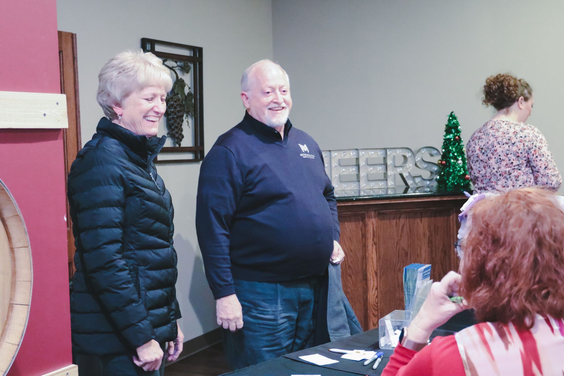 Two people smiling inside, near a table with a 