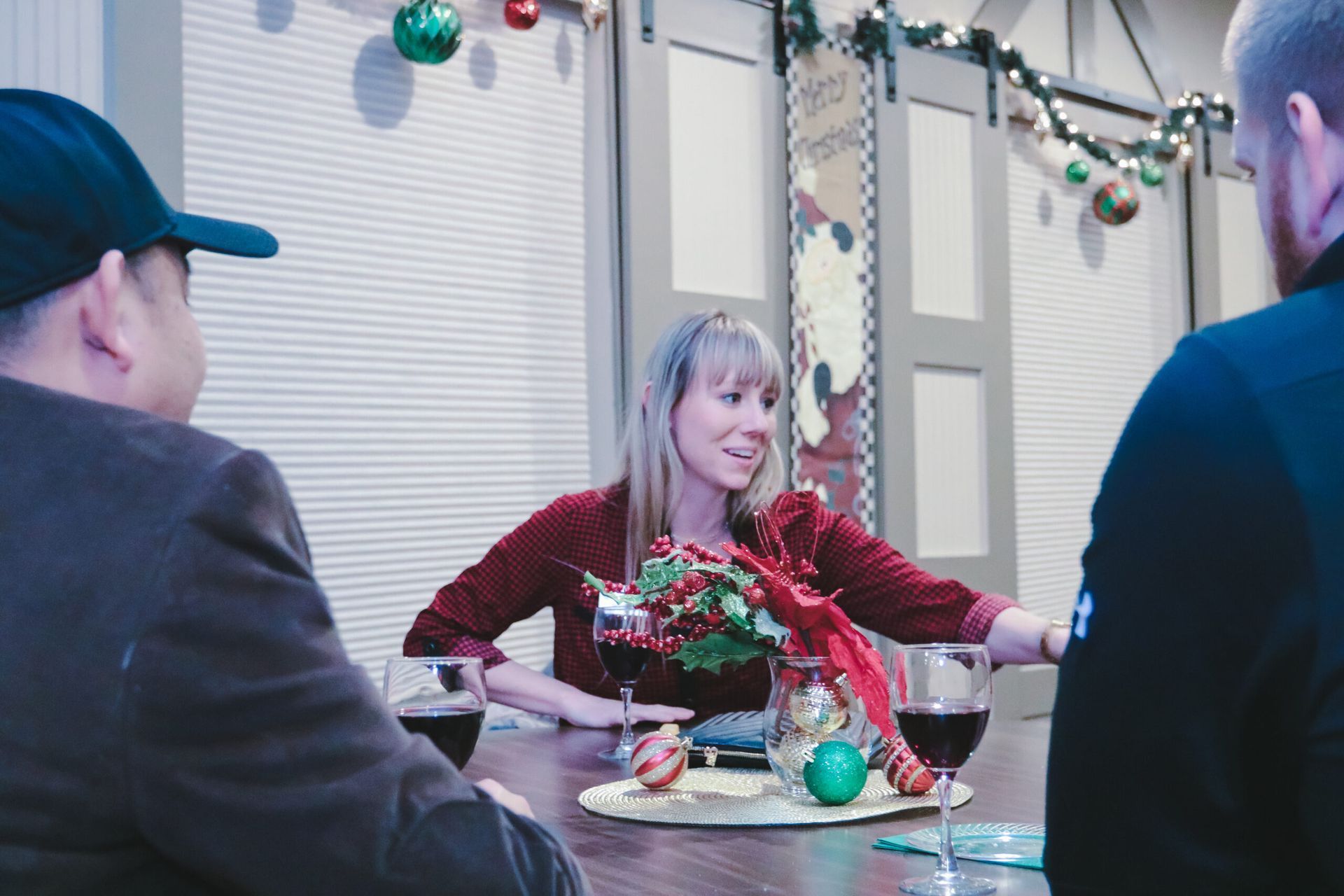 People at a decorated table, woman gesturing, drinks, Christmas ornaments.